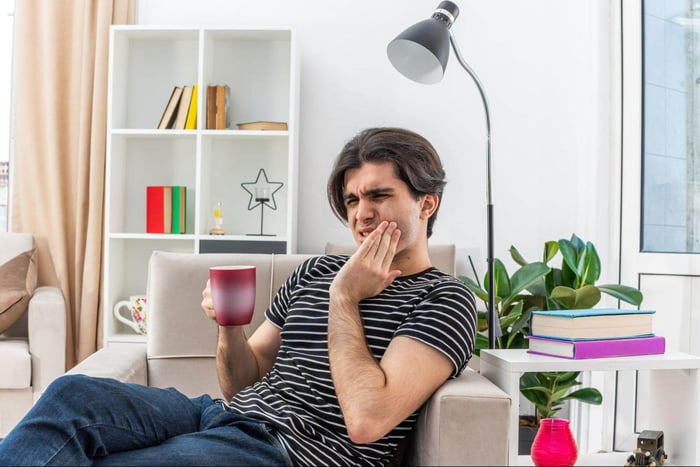 oung man holding mug looking unwell touching his jaw